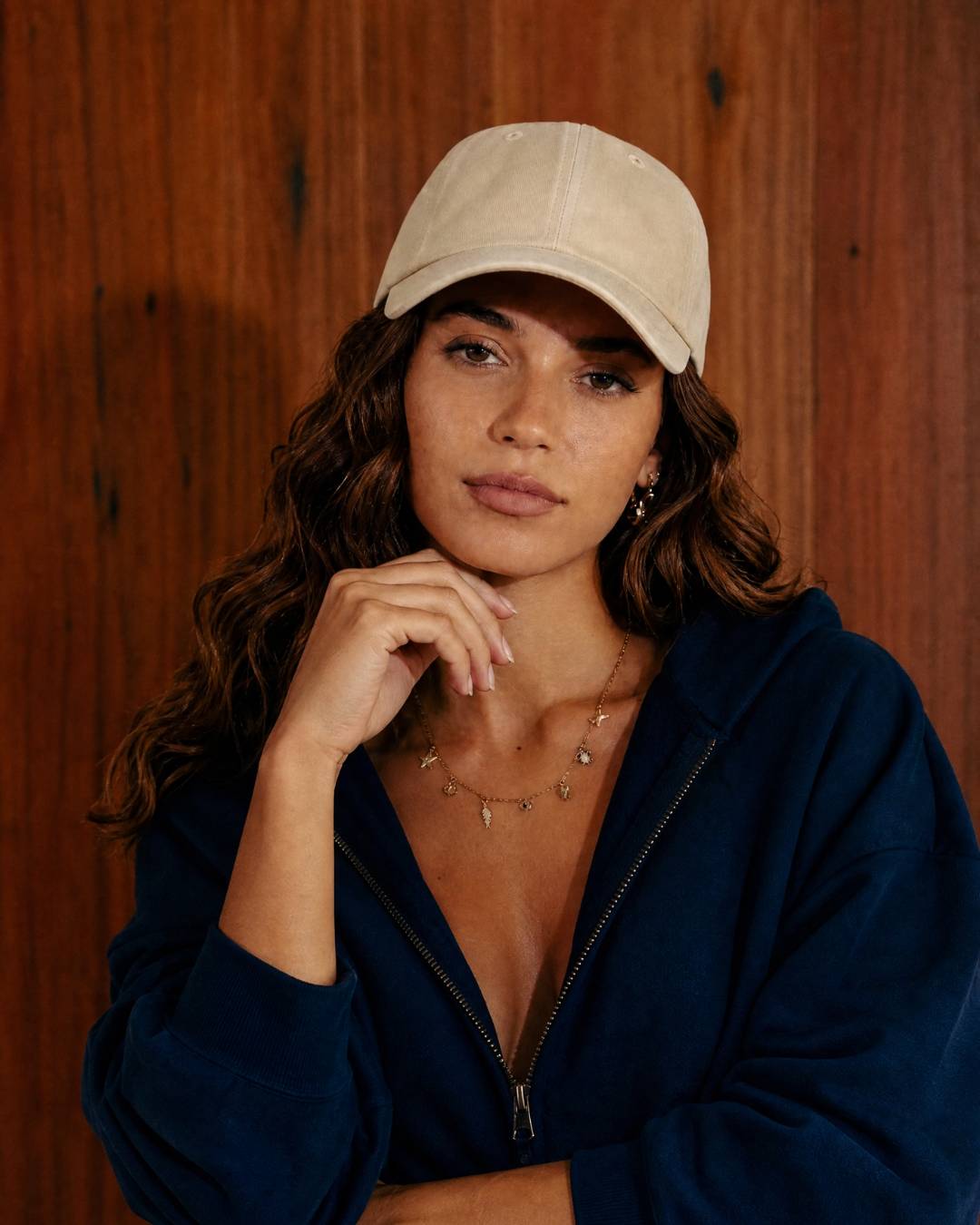 Woman wearing a beige cap and navy jacket against a wooden background