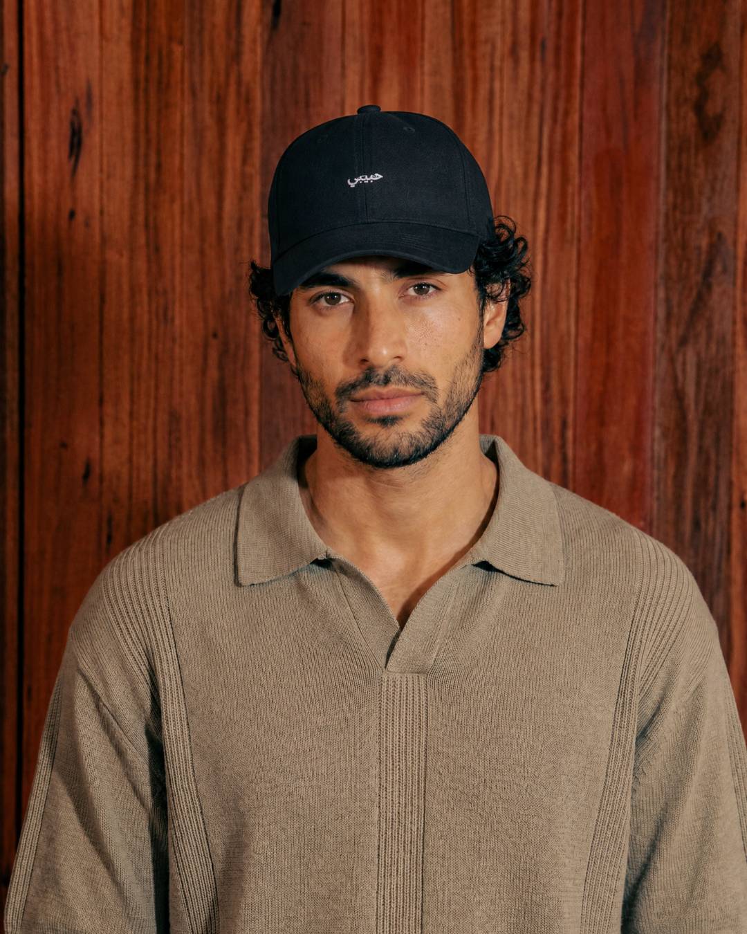 Man wearing a navy cap and beige sweater against a wooden background