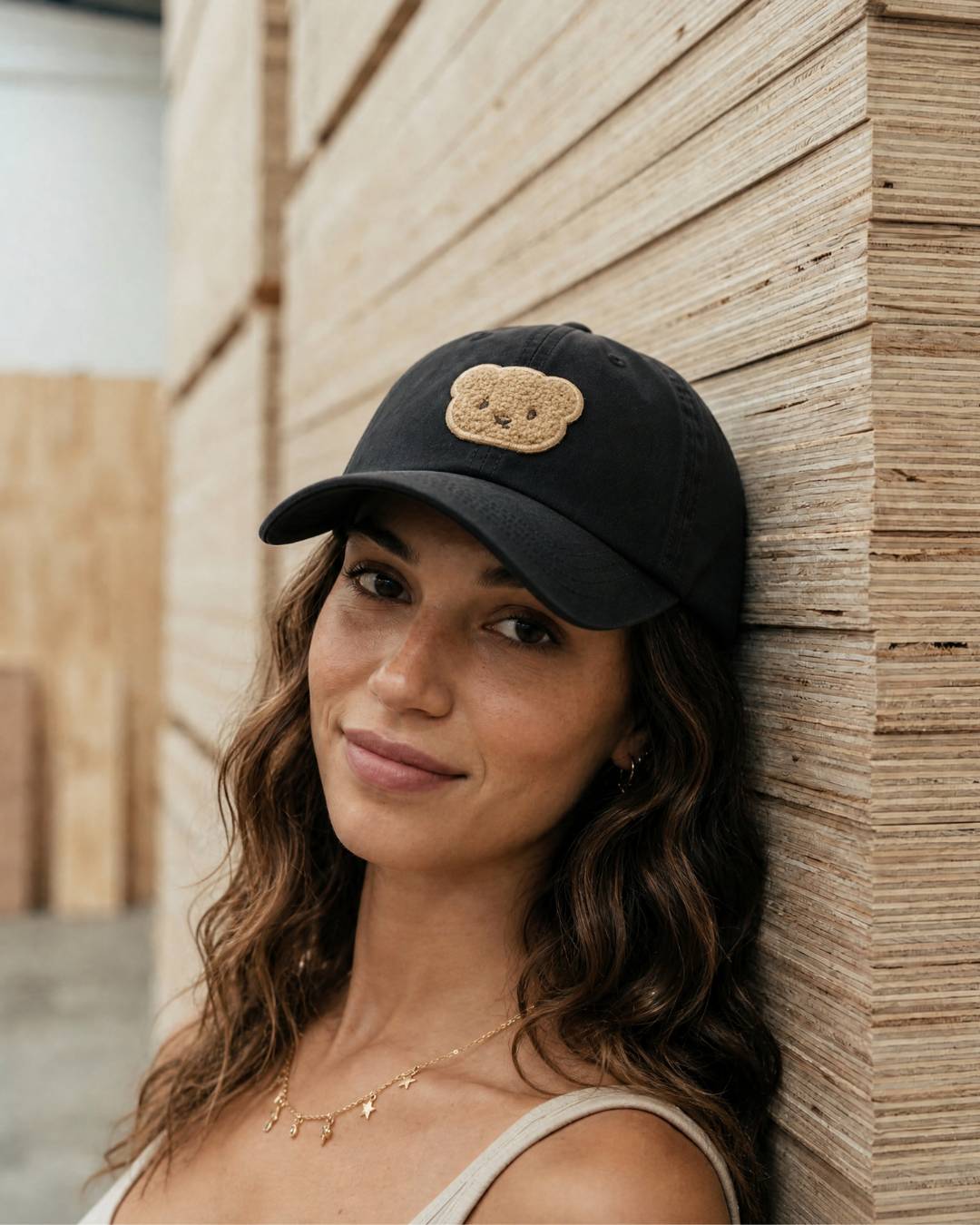 Woman wearing a black cap with a bear emblem against a wooden wall