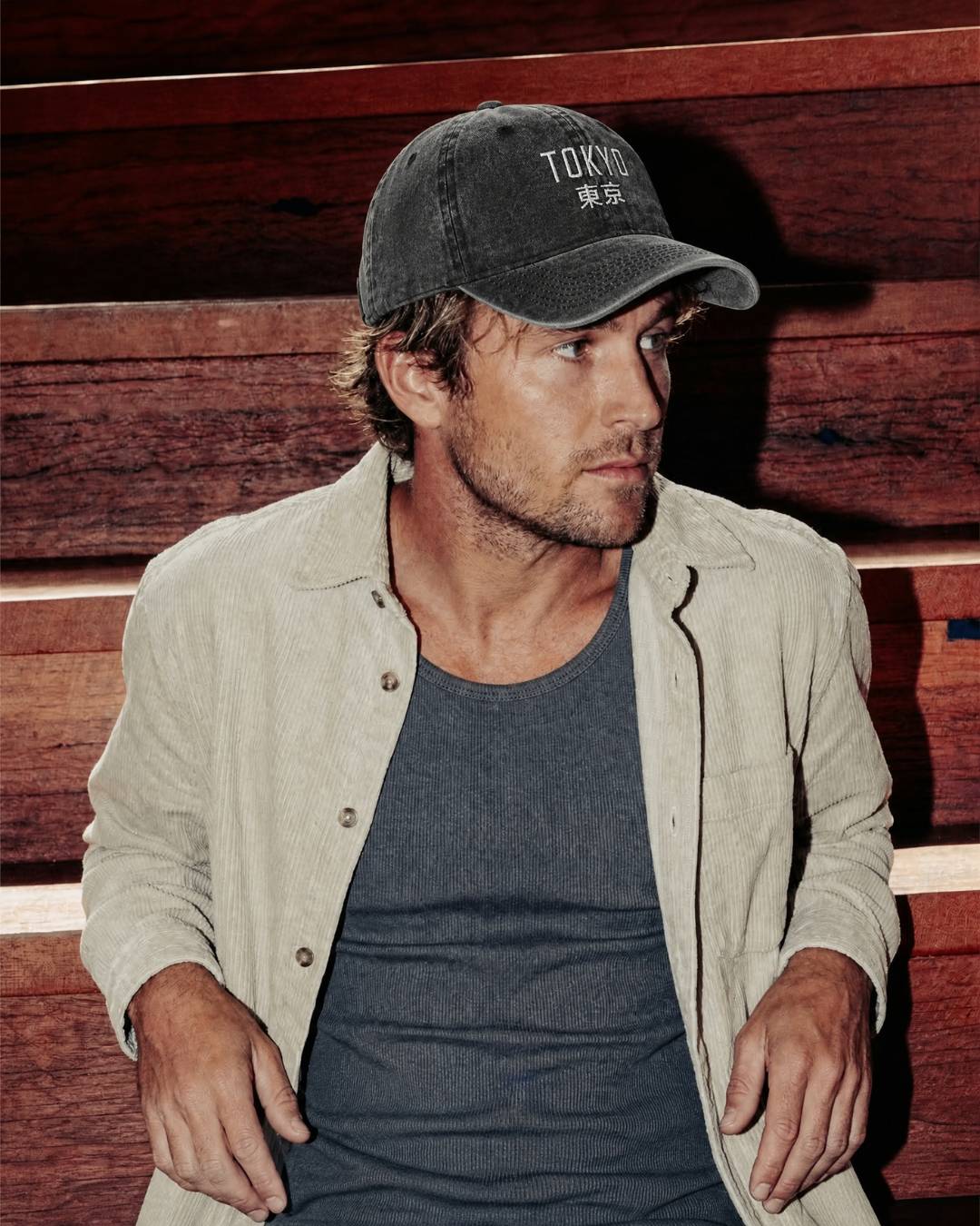 Man wearing a cap and light jacket against a wooden background
