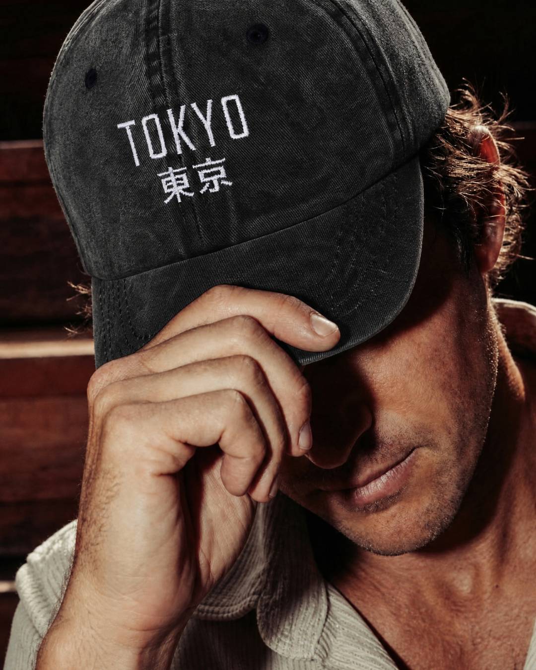Man wearing a black cap with 'TOKYO' and Japanese characters, resting his head on his hand.