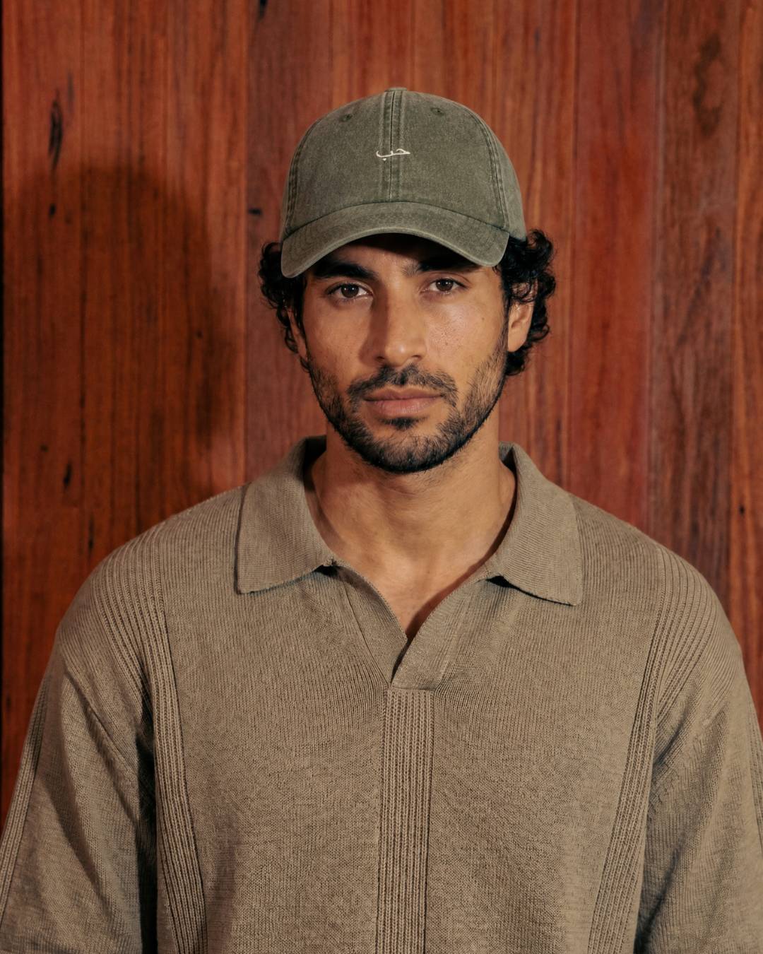 Man wearing a cap and brown shirt against a wooden background