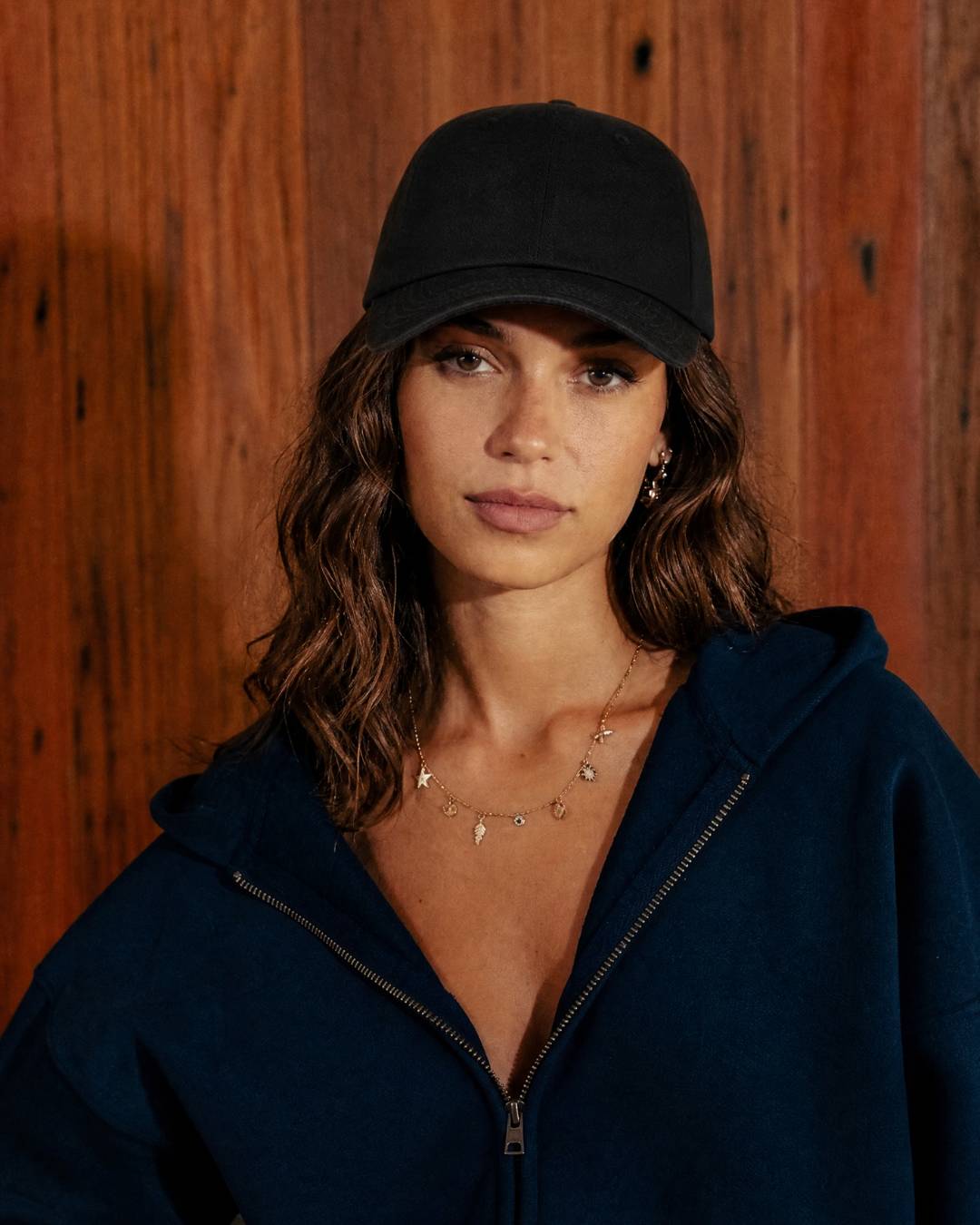 Woman wearing a black cap and navy hoodie against a wooden background