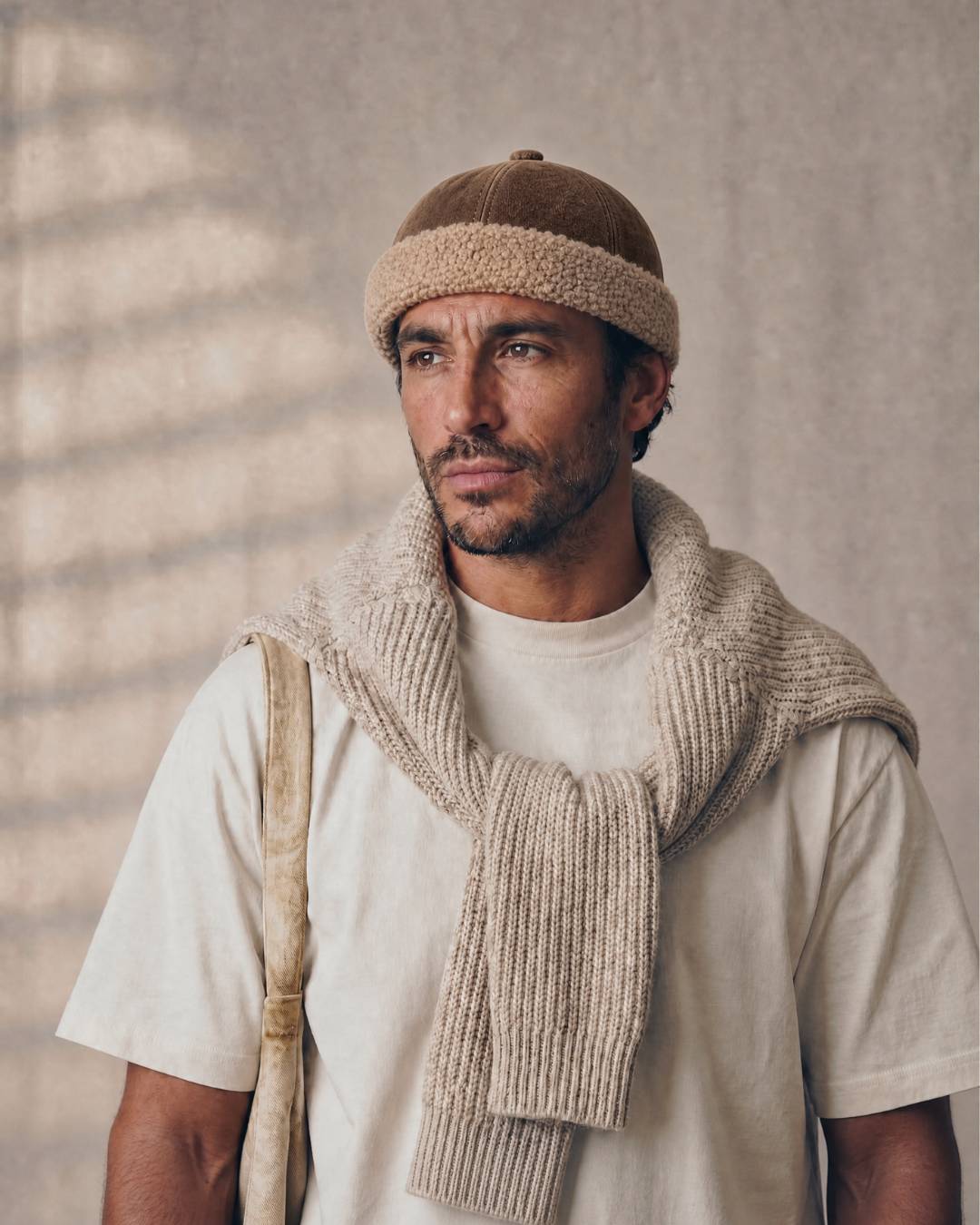 Man wearing a beige knit vest and hat against a neutral background