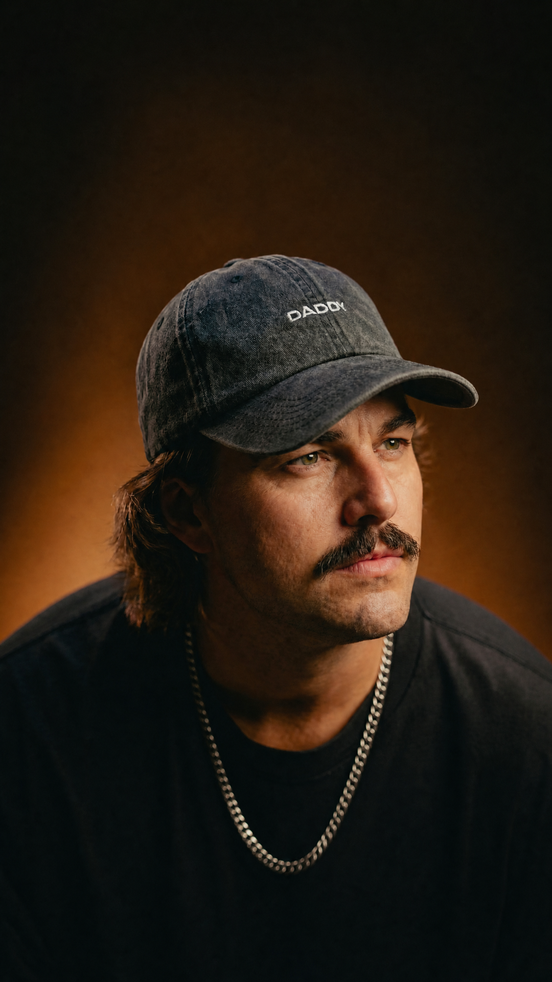 Man wearing CAPS Apparel Daddy dark blue cap against warm brown studio background