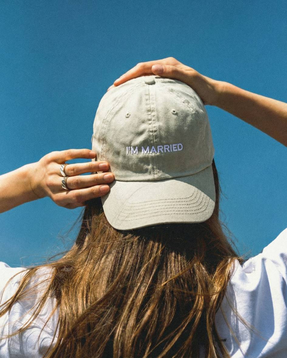 Person wearing a cap with 'I'm Married' text against a clear blue sky