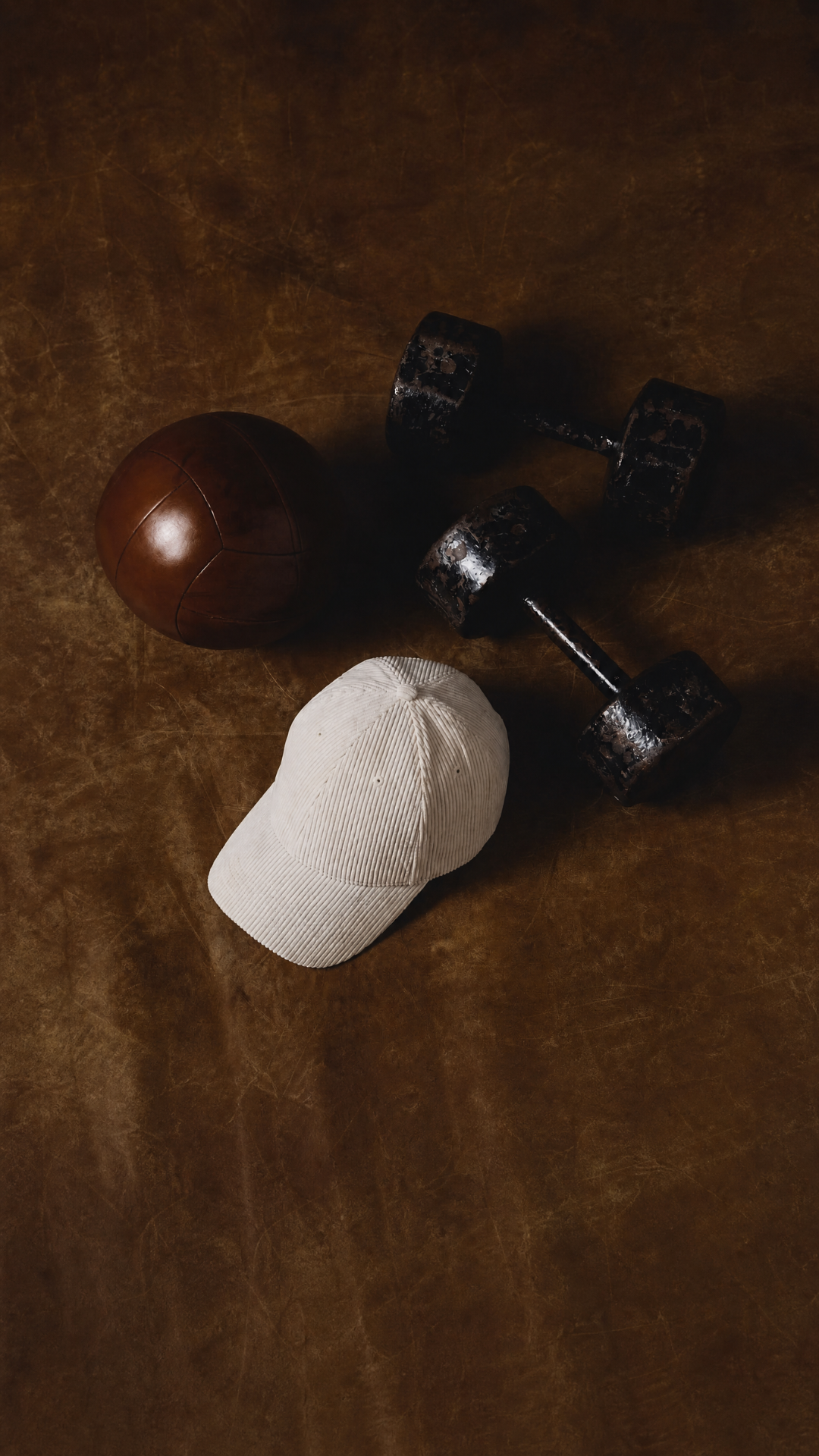 CAPS Apparel white corduroy cap with dumbbells and sphere on dark leather surface