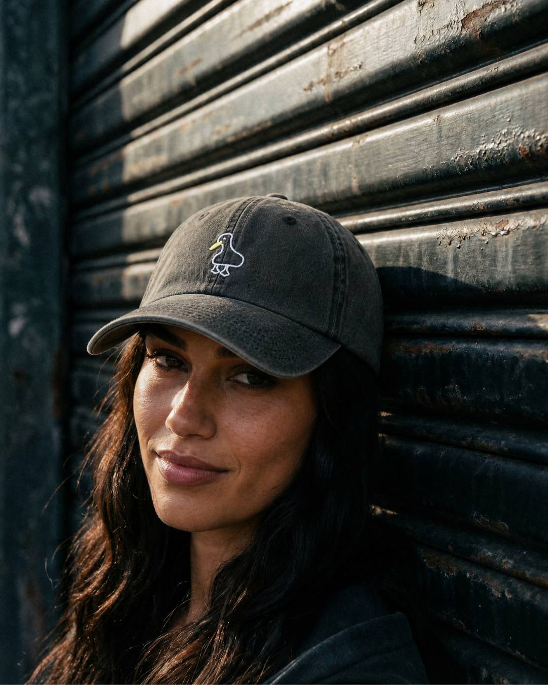 Woman wearing a black cap with a logo against a textured wall