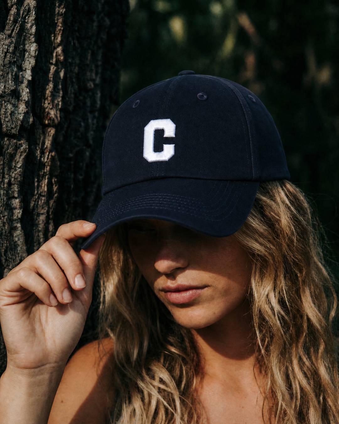 Person wearing a navy blue cap with a white 'C' logo, standing against a tree.