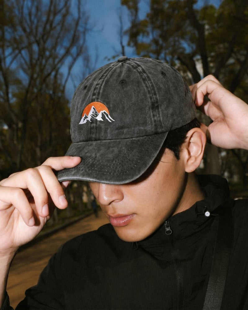 Person wearing a black baseball cap with a logo, outdoors.