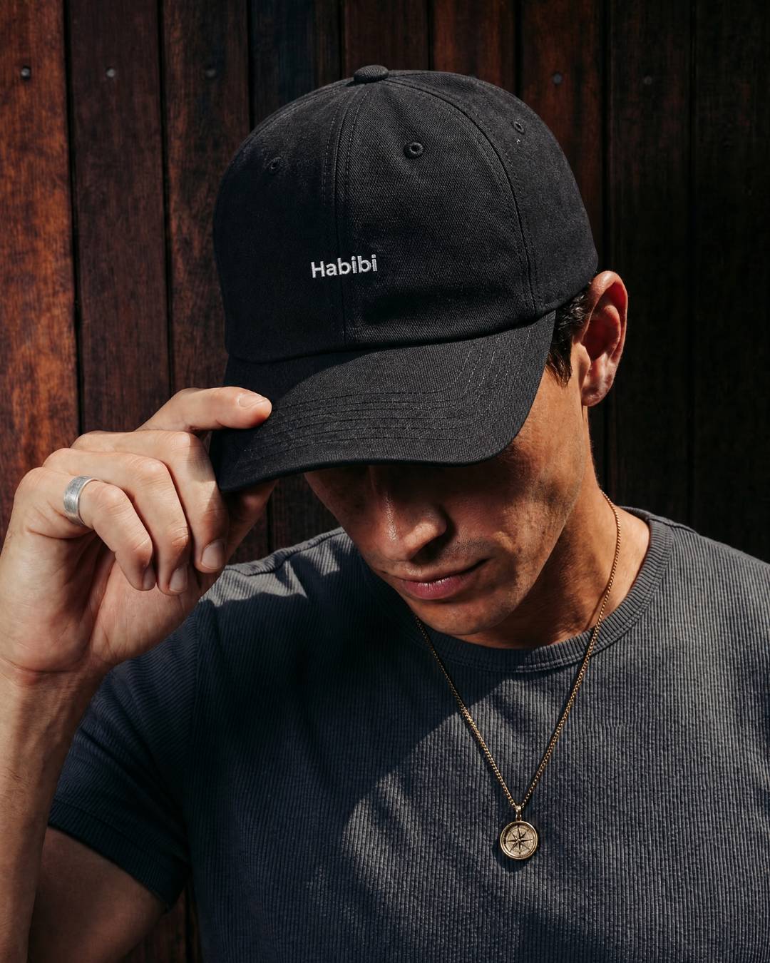 Man wearing a black cap with 'Habibi' logo against a wooden background