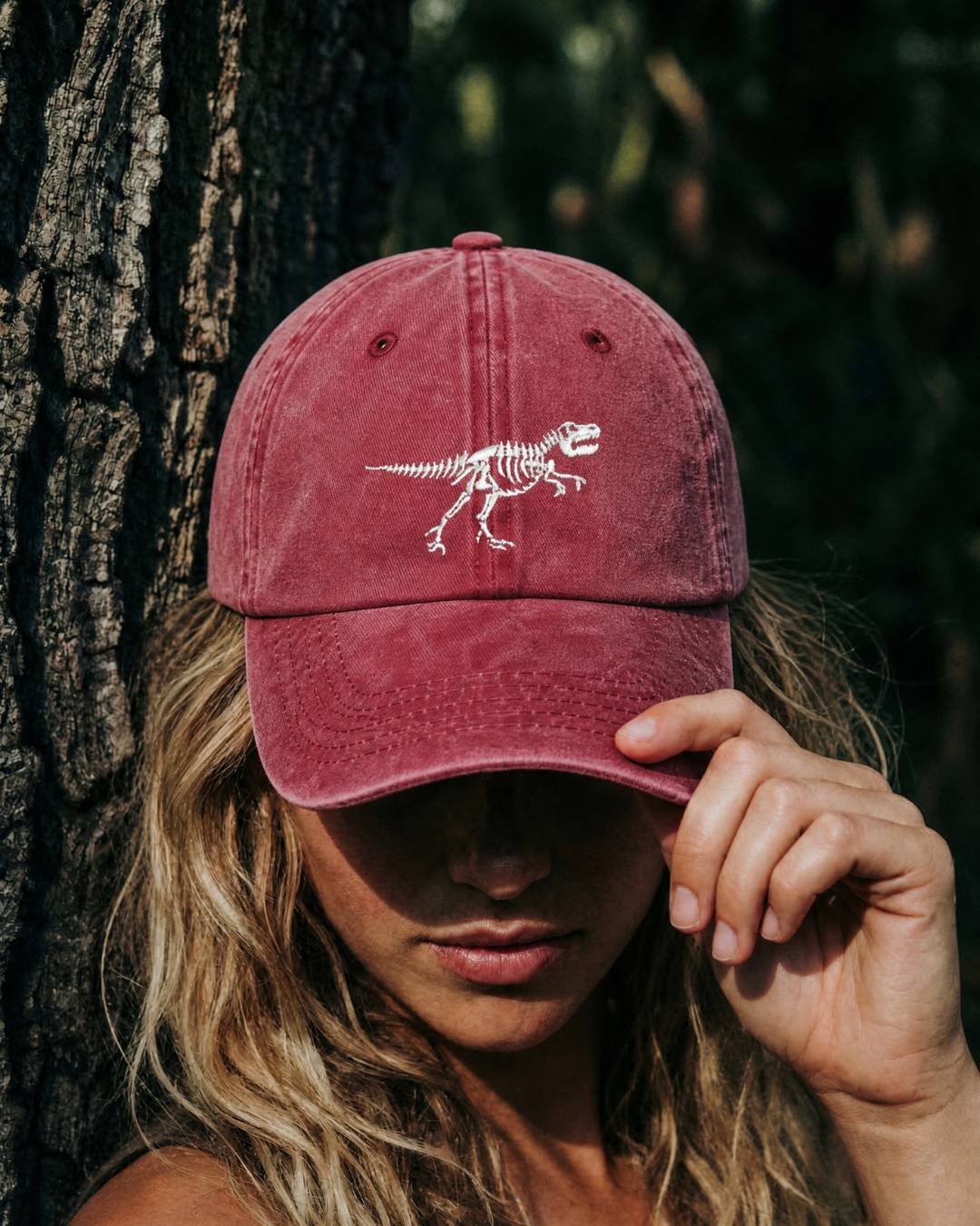 Person wearing a maroon cap with a dinosaur skeleton design against a natural background