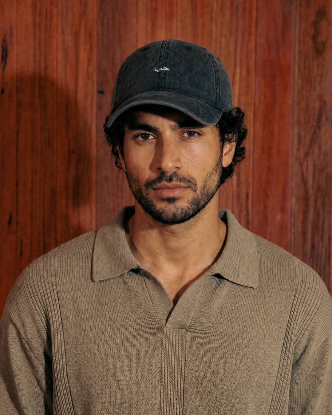 Man wearing a cap and beige sweater against a wooden background