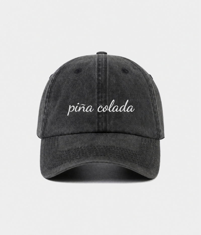 PINA COLADA - CURSIVE. washed black cotton dad cap with embroidered pina colada script, front view