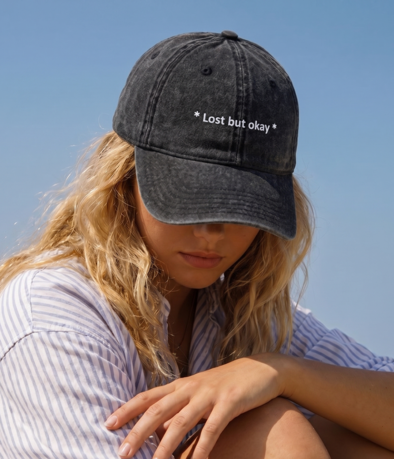 Persoon die een zwarte cap draagt met 'Lost but okay' tekst tegen een helderblauwe lucht