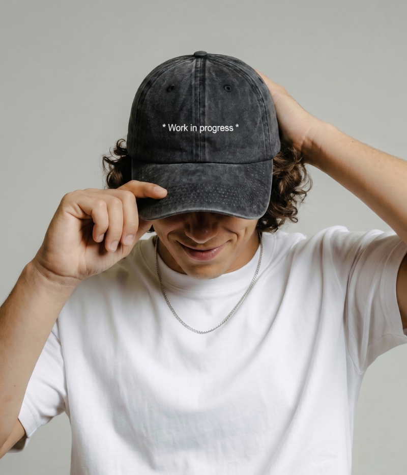 Person wearing a black cap with 'Work in progress' text on a plain background