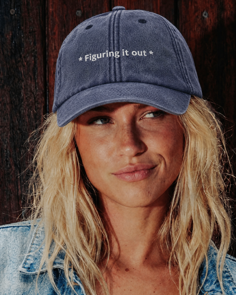 Woman wearing a blue Cap with 'Figuring it out' text against a wooden background