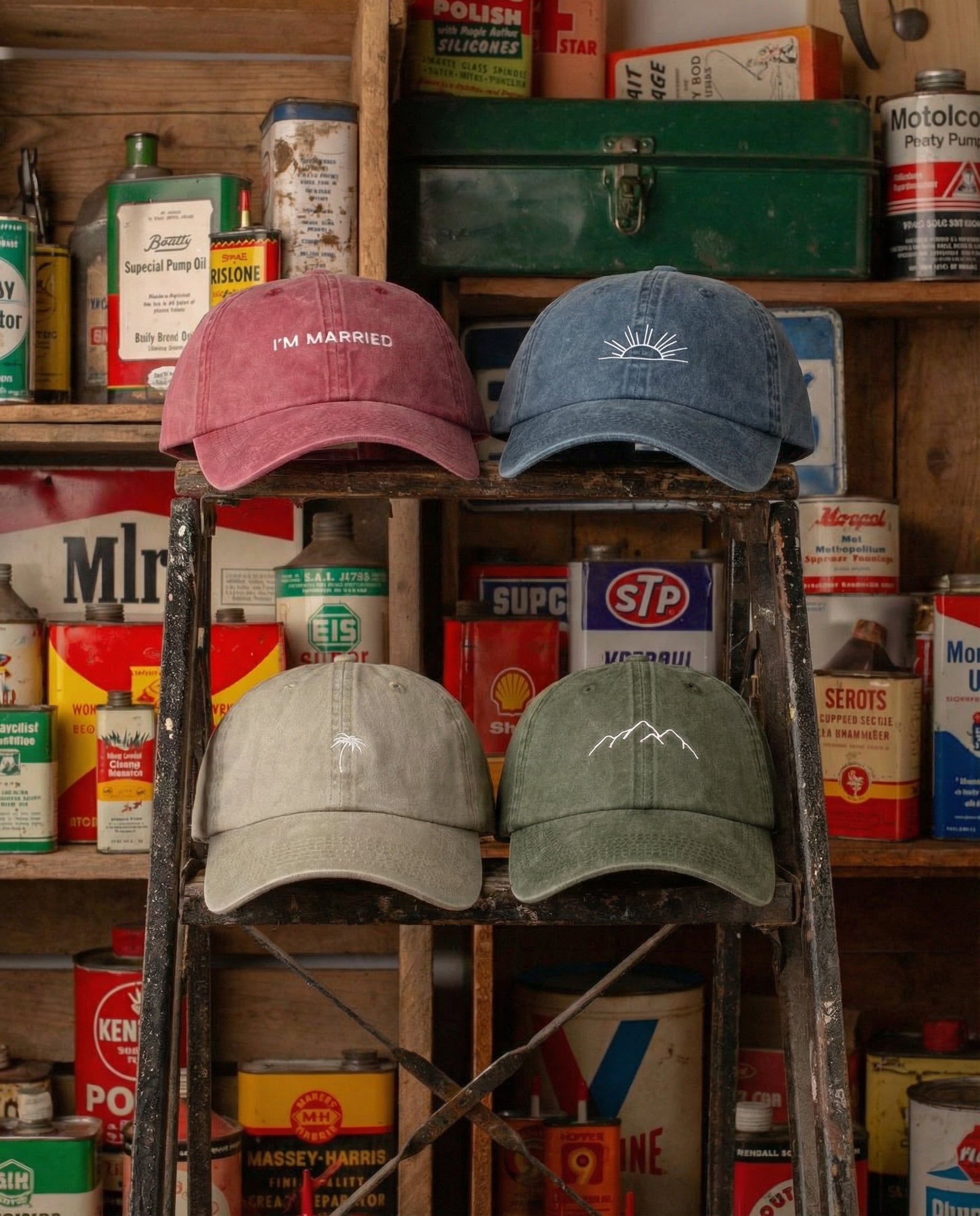 Four baseball caps on a ladder against a backdrop of vintage automotive supplies.